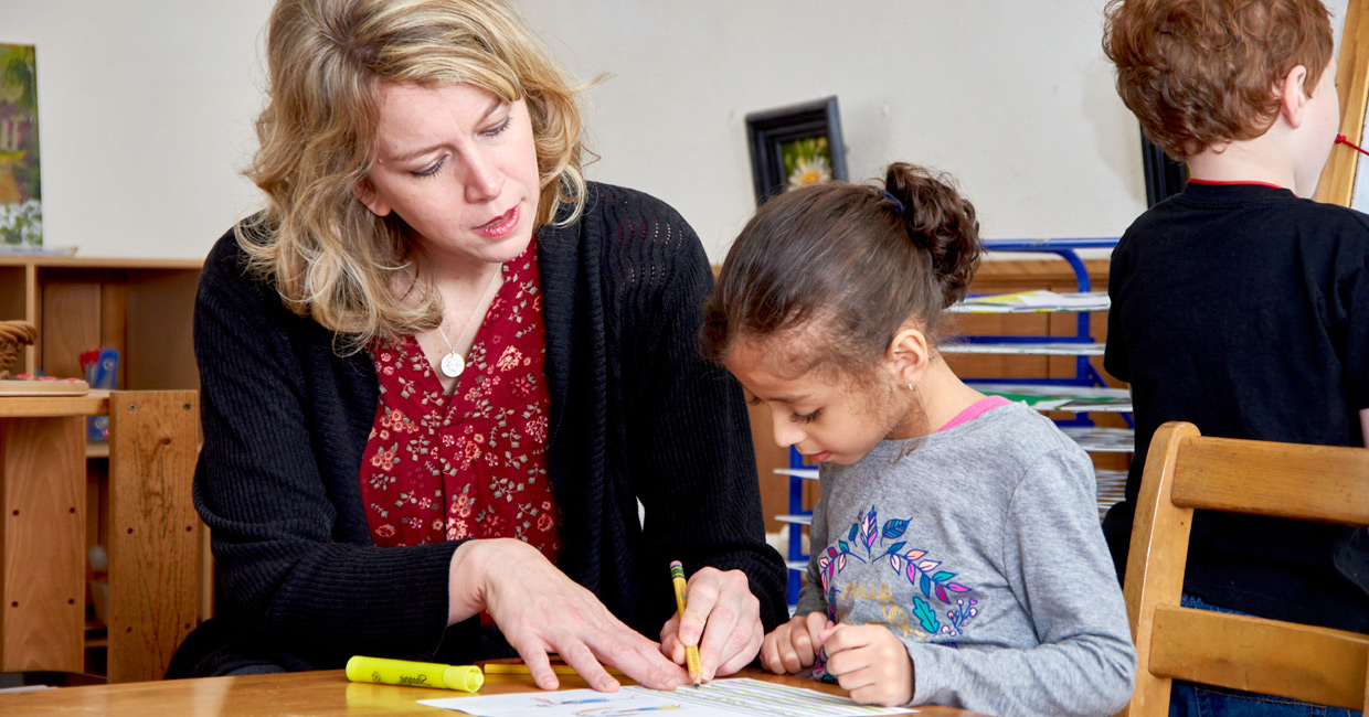 A Montessori guide using a marker to point at a paper for a student.